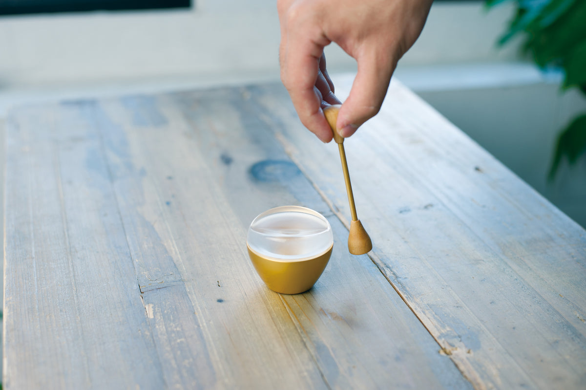 A hand tapping a brass orin bell with its small mallet